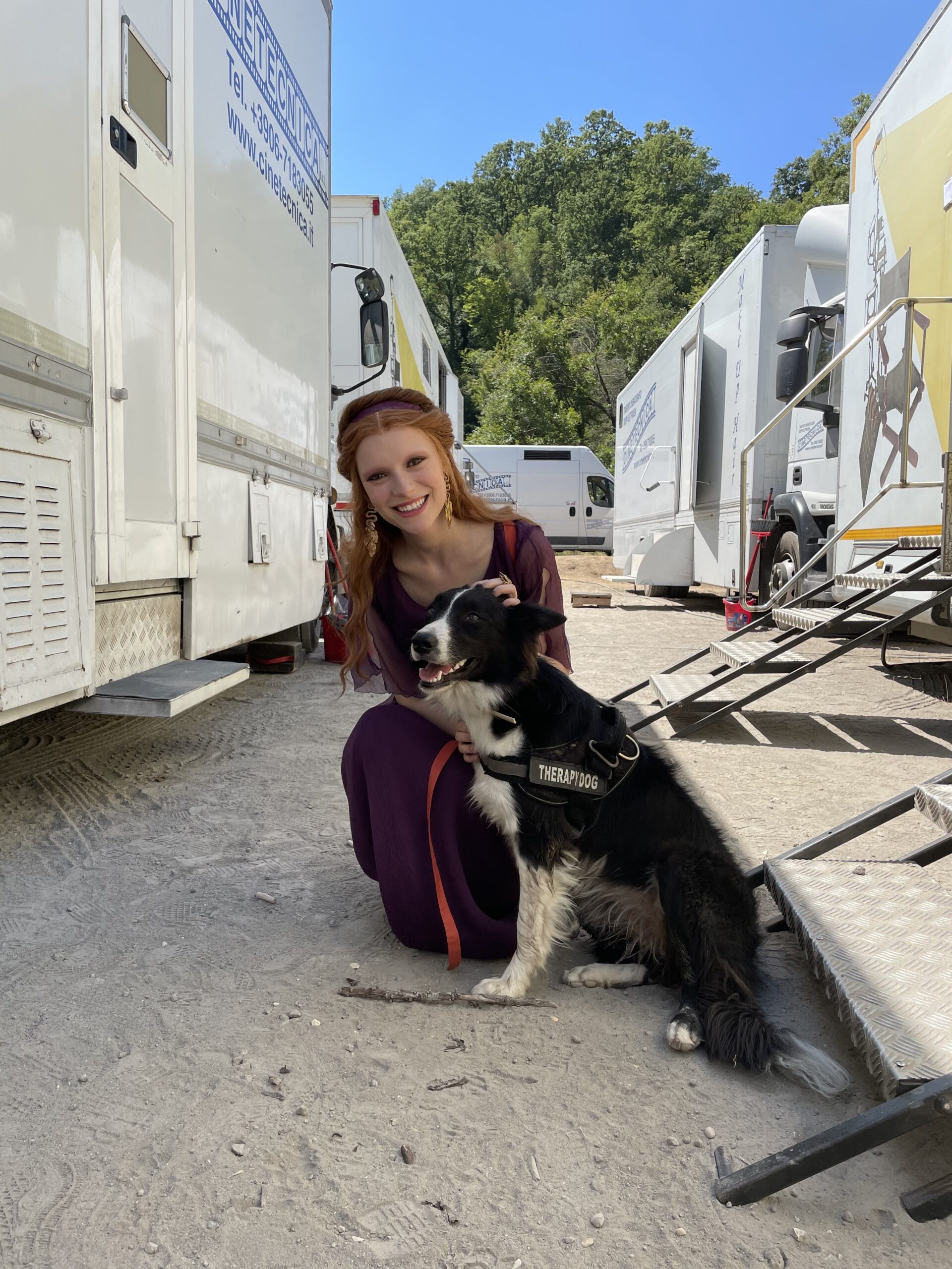 A behind the scenes picture of singer and actress Joelle dressed as the character Vipsania on the set of Domina season 2 cuddling a dog.